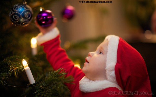 A toddler in a christmas costume reaching out for the baubles 